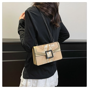 Detail of gold snakeskin pattern crossbody bag with black chain strap on a model
