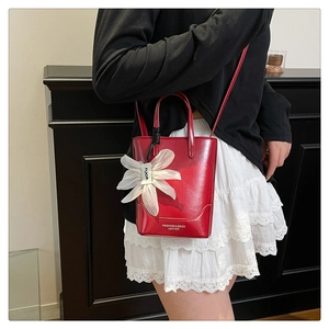 Detail of red leather bucket bag featuring a large white lace flower charm and crossbody strap