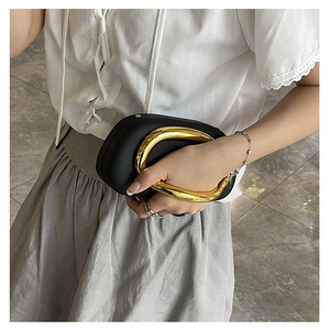 Detail of matte black capsule clutch with large round gold metal handle on model