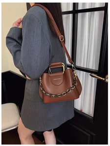 Brown leather bucket bag detail with chain strap on a model wearing a grey blazer