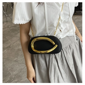 Detail of black mini evening clutch with large gold metal handle and chain strap