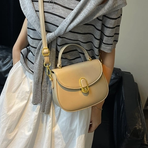 Elegant beige saddle bag with gold oval lock shown as a crossbody on a female model