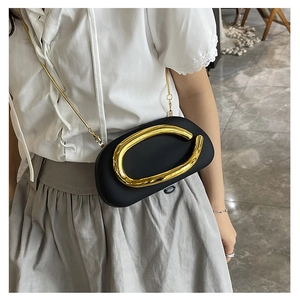 Detail of minimalist black oval clutch with gold irregular metal clasp and chain strap