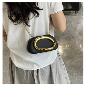 Street style shot of a black mini clutch with artistic gold metal handle and chain strap