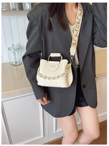 Detail of cream bucket bag featuring golden handle, acrylic chain, and patterned canvas strap