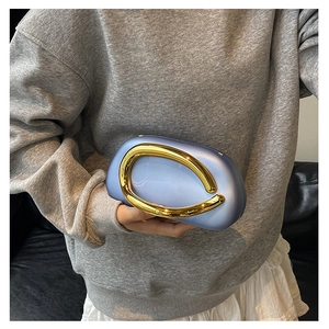 Detail of light blue clutch bag with sculptural gold metal handle held by model