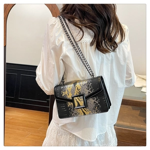 Detail of snake skin texture flap and gold metal buckle on a black crossbody bag