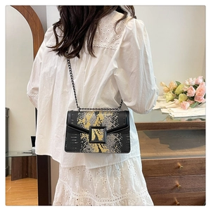 Detail of snake skin pattern crossbody bag with chain strap worn by a model