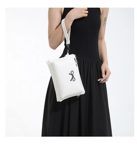 Close-up of white woven clutch bag featuring a black bow and wristlet strap