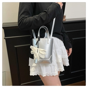 Detail of silver metallic bucket bag with white bow charm and adjustable shoulder strap