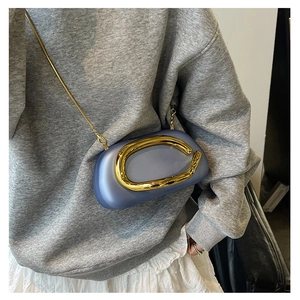 Close-up of a mini blue half-moon crossbody bag with gold ring and chain on model