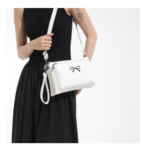 Close-up of white woven texture crossbody bag with a black metal bow buckle on model
