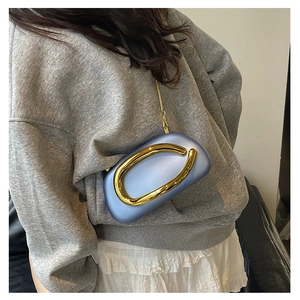 Detail of the blue oval clutch featuring a large gold metal handle and chain strap
