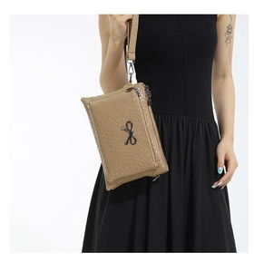 Detail of khaki woven texture handbag featuring black metal bow and zipper layers