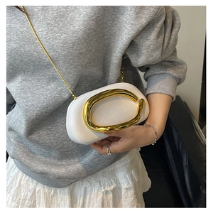 Macro shot of white oval evening bag with decorative gold C-shaped metal handle and chain