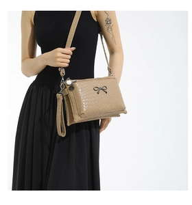 Detail of woven khaki crossbody bag with black bow hardware and multi-layer zippers