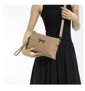 Detail of khaki woven texture bag with black bow clasp and detachable shoulder strap