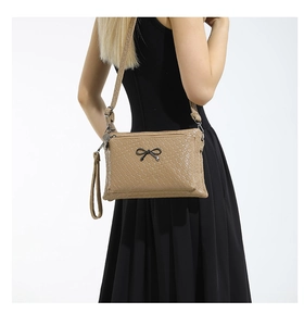 Detail of khaki woven texture crossbody bag with black metal bow and detachable straps