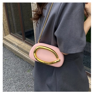 Detail of pink oval chain bag featuring a gold U-shaped handle on a gray blazer background