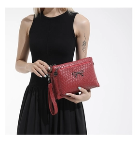 Detail of dark red woven texture handbag with black metal bow and multi-layer zippers