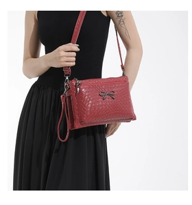 Detail of burgundy woven crossbody bag featuring a black metal bow and adjustable strap
