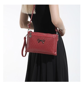 Detail of red woven texture handbag featuring black bow metal buckle and shoulder strap