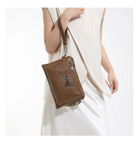 Detail view of woven brown leather clutch with metallic bow ornament and wristlet strap