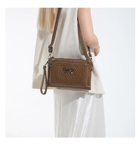 Detail of dark brown woven texture crossbody bag with metal bow and double zippers