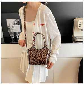 Close-up of leopard print handbag featuring cylinder handles and adjustable shoulder strap