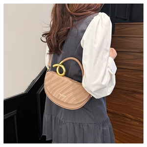 Detail of nude saddle bag featuring wavy texture and golden knot handle on grey vest