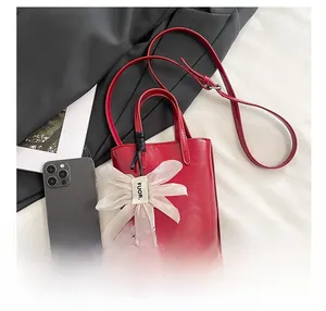 Detail of red leather tote bag with floral charm and phone for size reference