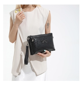 Detail of black woven handbag featuring a metal bow accent and detachable wrist strap