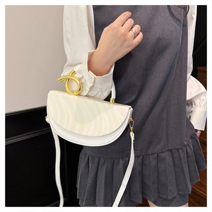 Detail of white semi-circle saddle bag with wavy texture and gold twisted metal handle
