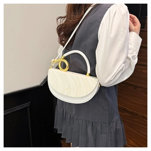Detail of white saddle bag with wavy flap design and elegant gold ring handle