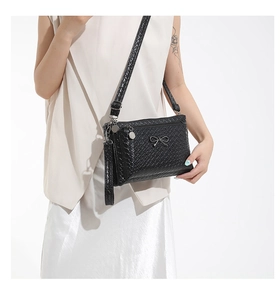 Detail of black woven texture crossbody bag with metal bow and triple zip compartments