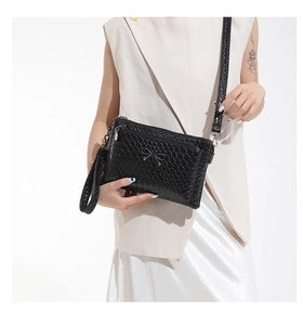 Detail of black woven texture handbag with metal bow accent and removable shoulder strap