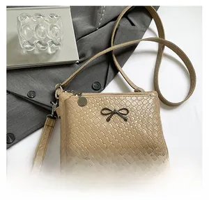 Close-up of beige woven texture handbag with metal bow detail and zipper closure