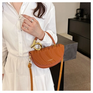 Detail of caramel half-moon saddle bag with rippled texture and golden ring handle