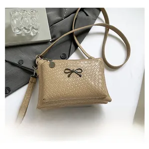 Khaki woven texture bag with metal bow shown next to a smartphone for size reference
