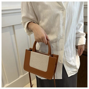 Detail of color-block canvas and brown leather crossbody bag held by a model