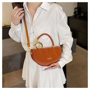 Detail of caramel half-moon saddle bag featuring unique golden twisted metal handle