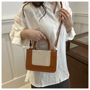 Detail of beige canvas crossbody bag with brown leather trim and white stitching