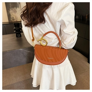 Macro detail of an orange semi-circle saddle bag with unique golden curved metal handle