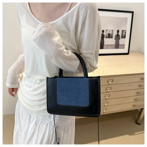 Detail of blue denim and black leather patchwork tote bag with cylindrical handles