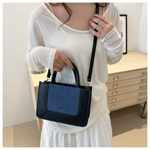 Detail of stylish two-tone denim and black leather crossbody bag with golden hardware