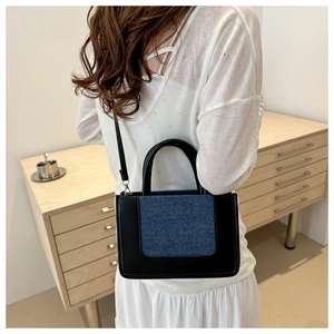 Detail of trendy canvas patchwork handbag featuring black PU leather and blue denim contrast