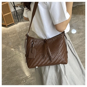 Close-up of the woven leather texture and crossbody strap on the brown bucket bag