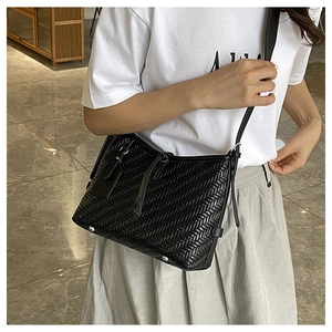 Detail of black woven leather handbag showing intricate texture and metal bottom studs