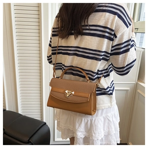Close-up of brown textured leather bag with gold lock and chain detail on casual outfit