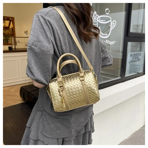 Golden woven Boston bag shown with adjustable shoulder strap in an outdoor cafe setting